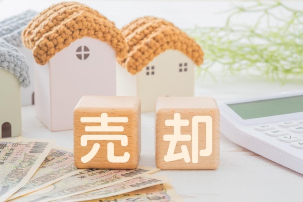 売却と書かれた木のブロックと家の模型、日本円の紙幣や電卓