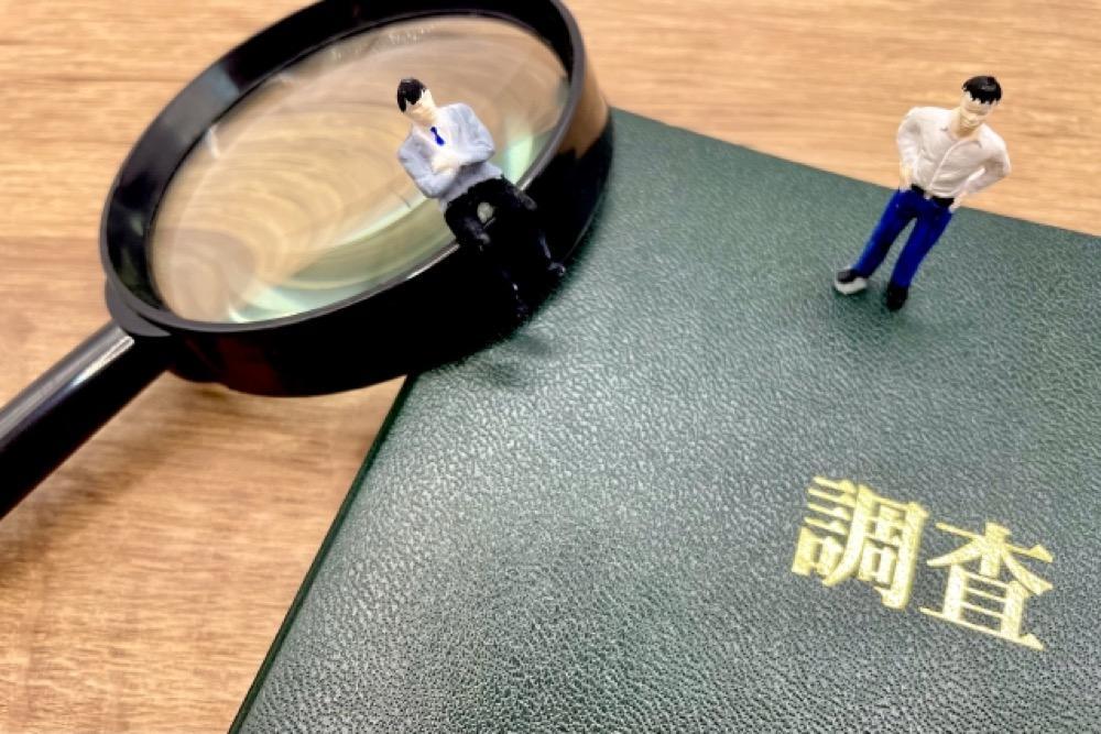 調査と書かれた書類の上に置かれた虫眼鏡とミニチュアの人物たち
