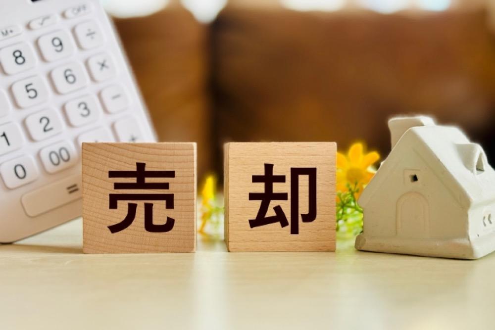 売却に関する木製ブロックと家の模型、電卓が並ぶ不動産イメージ