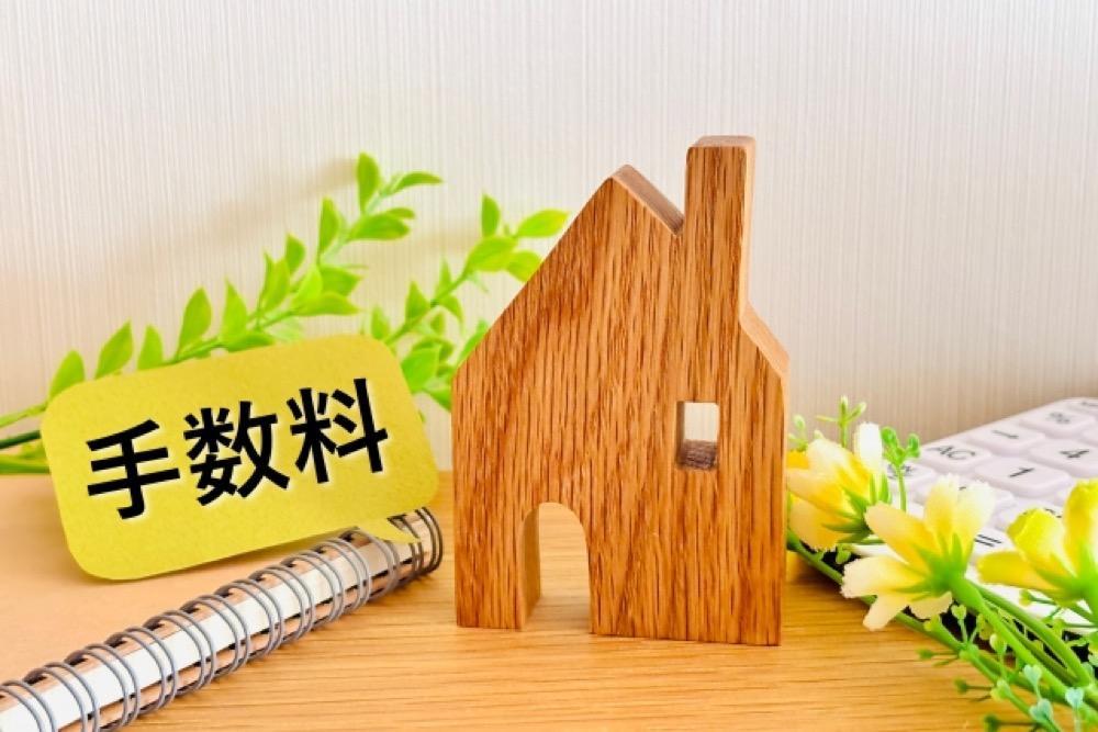 不動産売買の手数料を表す札と木製の家の模型イメージ