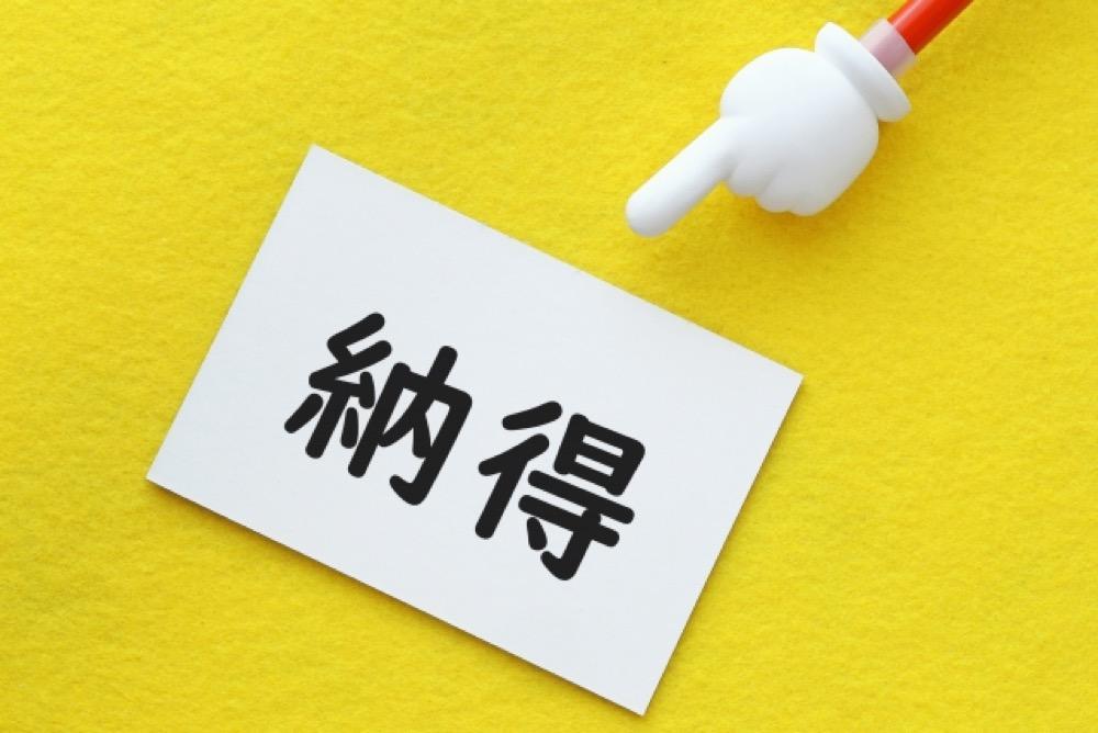 黄色い背景に「納得」と書かれたカードを指差す手のイラスト付きペン
