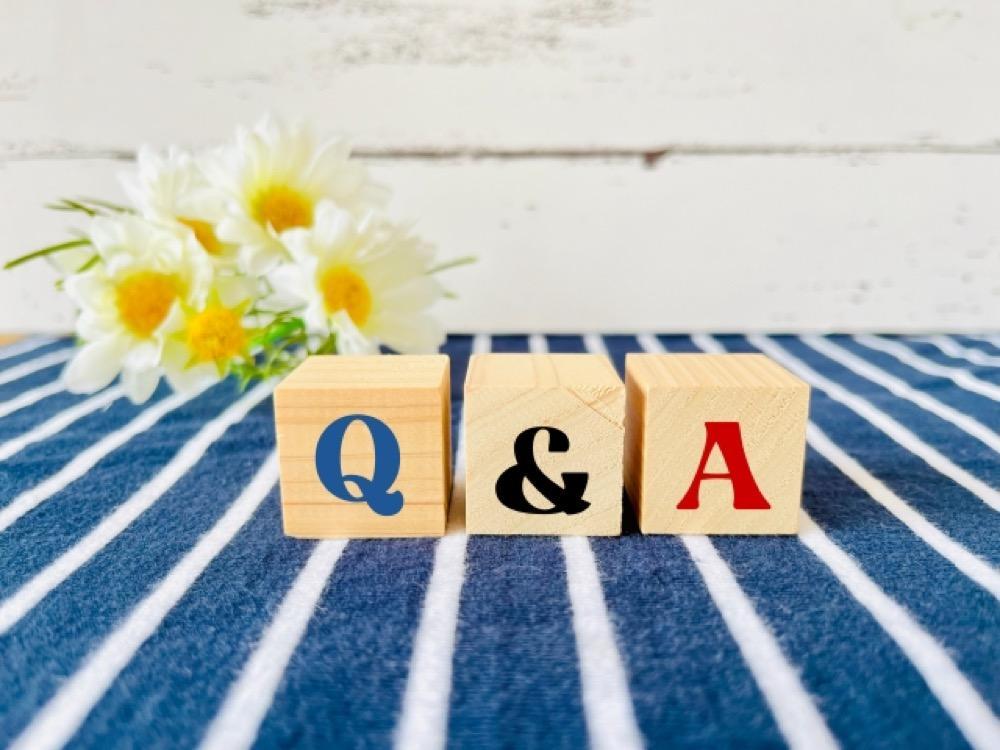 青と白のストライプの布の上に「Q&A」と書かれた木製ブロックと白い花